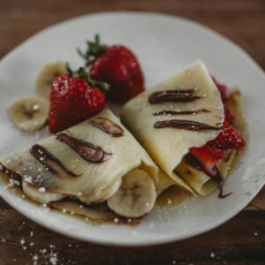 Tasty French crepes topped with fresh strawberries, bananas, and Nutella sauce.